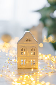 Soft Christmas scene with white ceramic house, glowing warm fairy lights and neutral winter decor. Cozy minimalist holiday background perfect for seasonal designs.