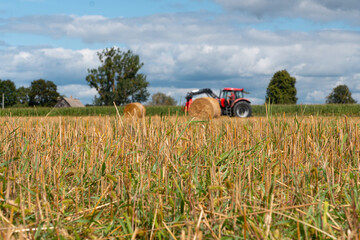 Red tractor working in a harvested agricultural field, farm machinery for farming and crop production under dramatic cloudy sky © Iryna