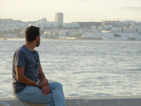A white, dark-haired, thin man of 40 years old with an introspective expression. A white, dark-haired, thin man of 40 years old with an introspective expression, is in an urban environment near a rive