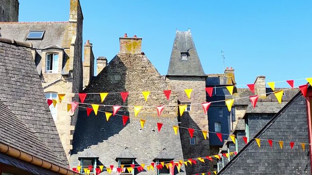 Colorful red and yellow pennant flags hanging above a narrow street between historic stone buildings. Perfect for festival invitations, street party videos and travel guides.