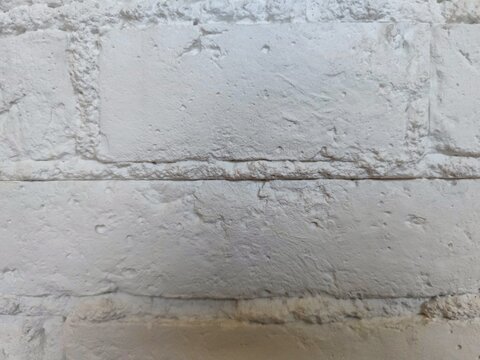 Full frame background texture of uneven white painted brick wall with thick mortar

