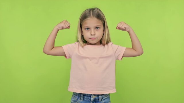 A young girl flexing her muscles, with a determined look on her face. She is wearing a pink shirt and has short hair. The background is a plain, bright color.