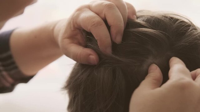 Close-up child's head with female hands searching for lice and nits in hair, combing through with orange comb for removal, Pediculosis, regular hygiene and pest control