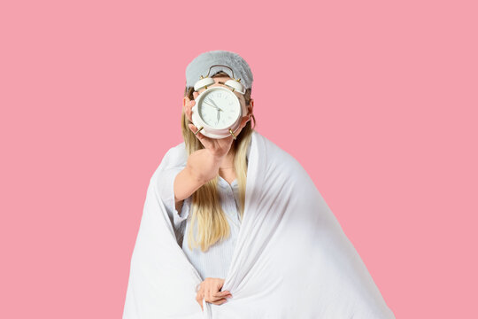Young woman with white blanket and alarm clock on pink background