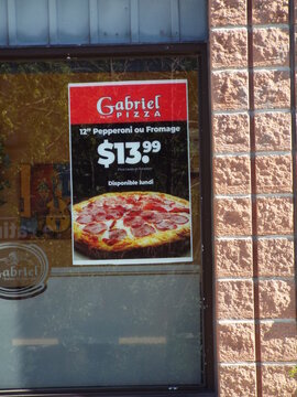 Gatineau, Quebec, Canada &ndash; June 24, 2026: A Gabriel Pizza storefront window features a promotional poster advertising a "Monday pizza special for thirteen dollars ninety-nine" on Bd Gr&eacute;ber.