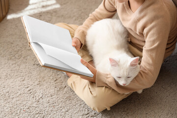 Naklejka premium Cute little boy with cat reading book on carpet at home