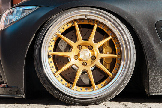 Side view of tuned BMW 4 Series F32 coupe with custom golden SSR Professor MS3 forged alloy wheel rim, luxury matte black stance automobile parked near brick wall, automotive tuning industry. 