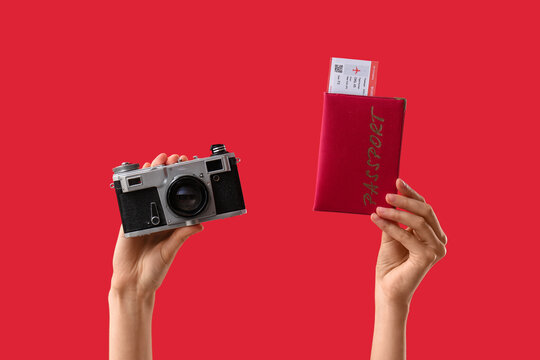 Female hands with photo camera, passport and ticket on red background, closeup