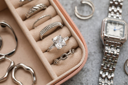 Open organizer with different silver jewelry and wristwatch on grey grunge background, closeup