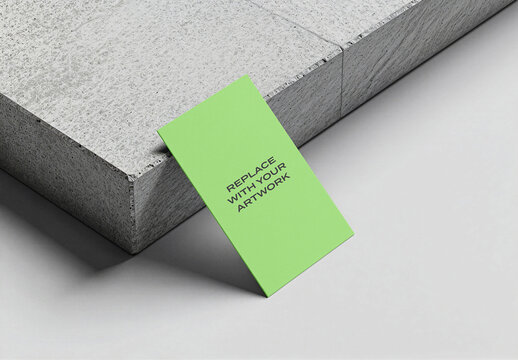Business card mockup leaning against a textured concrete block on light gray surface, realistic stationery branding presentation with clean studio lighting and minimalist composition, template