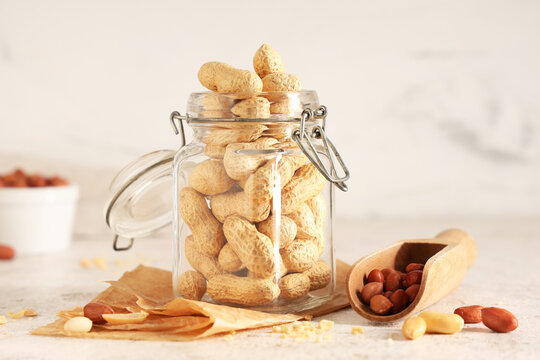 Glass jar and scoop with peanuts on light table