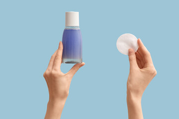 Female hands with cotton pad and bottle of micellar water on blue background © Pixel-Shot