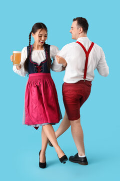 Young happy couple in traditional German clothes with mug of beer dancing on blue background