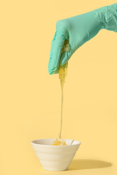 Beautician hand with sugaring paste on pale yellow background