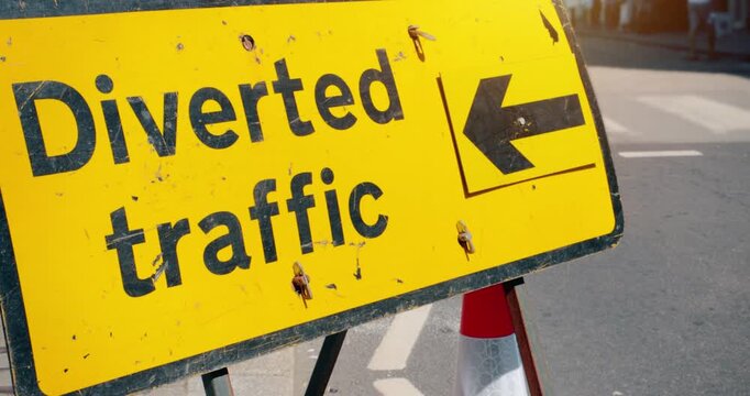 Road closed - Diverted traffic highway road sign in the event of a roadblock. Travel safety on closed street with arrow on yellow high visibility signage marking temporary closure.