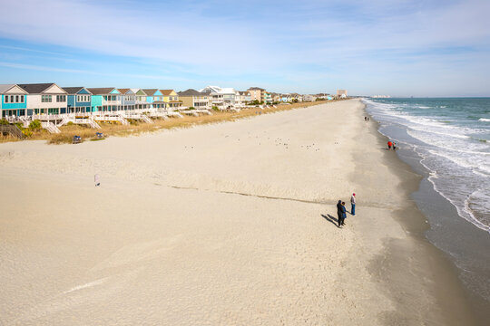 Winter view of colorful beachfront homes along the dunes and sandy beach at the Grand Strand coastline of Surfside Beach, South Carolina, with the Myrtle Beach skyline in the distance.