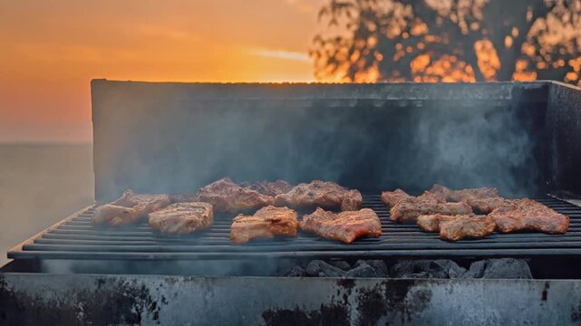Juicy Meats Sizzling on Outdoor Charcoal Grill at Sunset with Swirling Smoke, Wide Shot Cinematic Full HD Footage