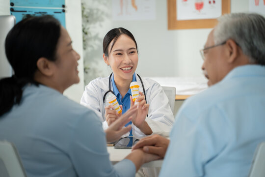 Smiling Asian female doctor in a white coat providing a positive health consultation to an elderly couple in her modern clinic office, with the senior man and woman holding hands.Concept of geriatric