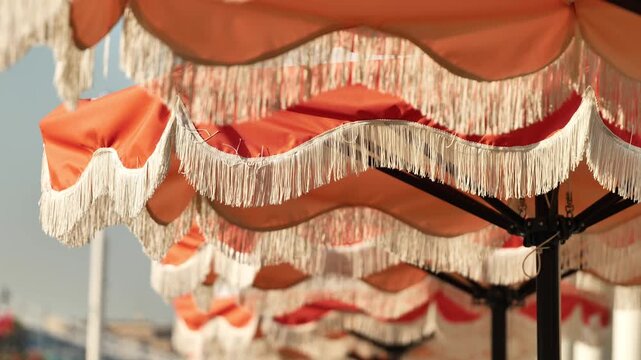 Row of classic orange fringed beach umbrellas providing shade on a sunny day