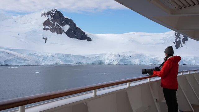 Beautiful Female Photographer Antarctica Cruise Ship Passenger in Orange Coat on Deck. Looks Out Epic Adventure Travel Snow Covered Mountains.