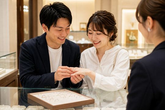 婚約指輪を試着するカップルとスタッフ