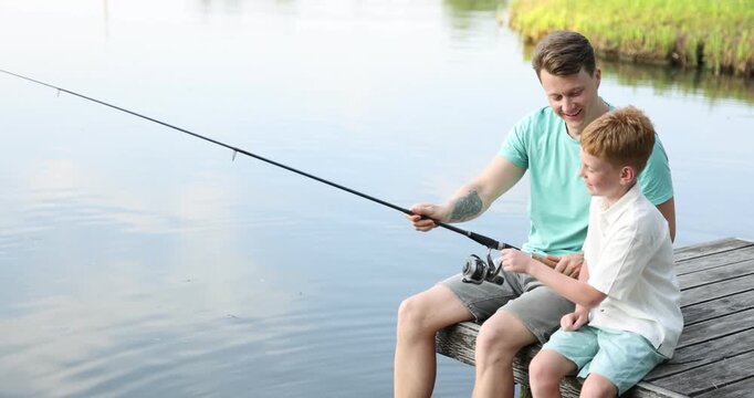 Father and his little son fishing together near river outdoors