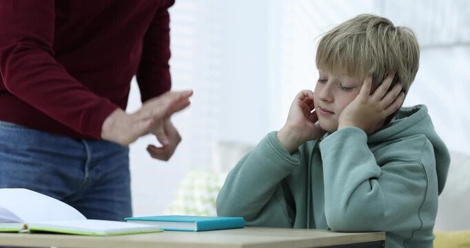 Father scolding his son while helping with homework at wooden table indoors, closeup