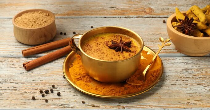 Woman adding anise star to golden milk turmeric latte and taking cup of drink from old wooden table, closeup