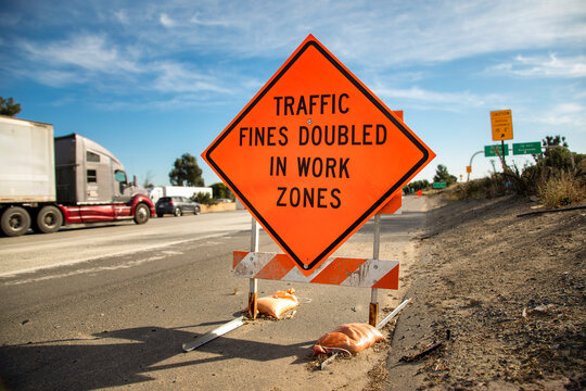 Orange traffic sign stating Traffic Fines Doubled in Work Zones with traffic in the background. The image is from the 15 freeway in Escondido Ca