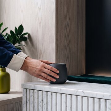 Close-up of hands placing a modern matte black ceramic cup on a fluted marble countertop in a stylish interior
