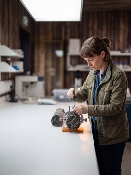 Female geologist examining and measuring a volcanic rock core sample with precision tools in a science laboratory