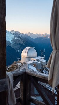 High altitude astronomical observatory dome framed by wooden terrace overlooking alpine mountain range