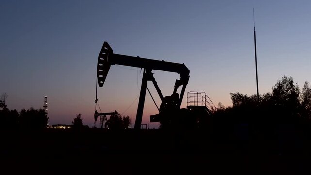 Oil extraction in oil field on evening sunset. Extraction of petroleum in night. Crude Oil Production. Crude pump jack working on oil field. Crude Pumpjack on sunrise. Industrial petroleum industry.