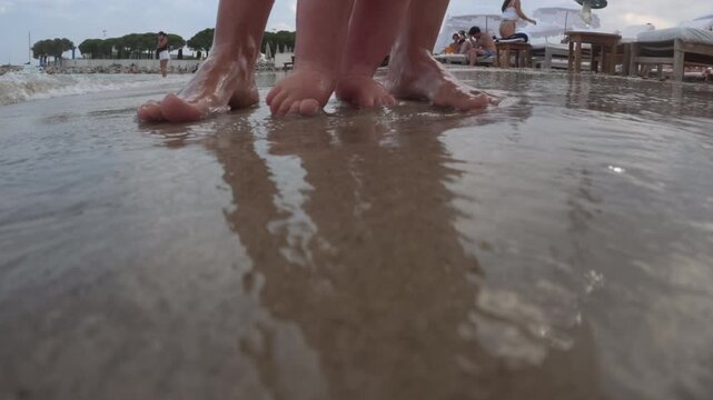 Adult and baby feet exploring the shallow ocean water on a sandy beach, enjoying family vacation moments in summer
