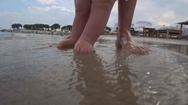 Baby feet and adult feet standing in gentle ocean waves on a sandy beach, enjoying the summer vacation and family time