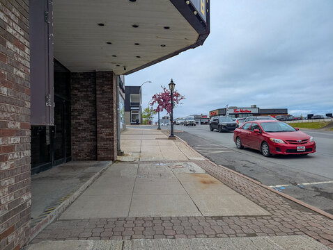 Gaspesie, Quebec, 06 June 2026 : Cars drive on an urban street past a building and flowering tree, with a Tim Hortons restaurant visible.