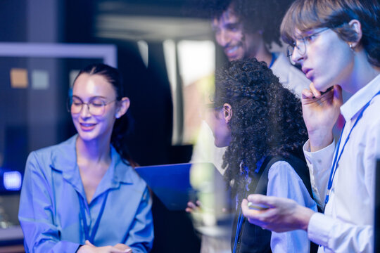 Candid moment as a diverse, multiethnic software team share reports as a standing team in a modern technology office bathed in blue light, showcasing a diverse, multiethnic team (frame 944)