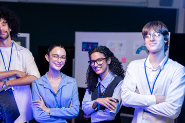 Fototapeta premium Wide shot of a diverse, multiethnic software team stand arms crossed for the group photo against a deep-blue studio backdrop, capturing collaboration on an inclusive engineering team