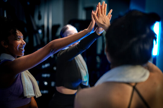 Female strength training: two female workout partners sharing a high five in a dark modern gym, captured in a cinematic fitness portrait, a scene of health and motivation