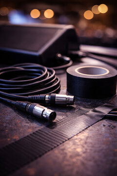Professional XLR audio cable with roll of black gaffer tape on stage floor and sound equipment with warm bokeh lights, live concert production and event setup concept