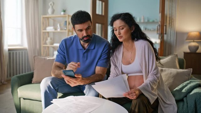 Expectant parents reviewing bills phone home. Pregnant wife husband finances.