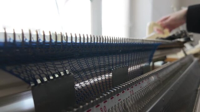 Close-up footage of automated knitting machine working with blue yarn creating mesh fabric.