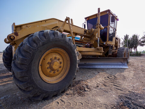 Low angle view of yellow motor grader machine working on dirt road leveling at construction site.Heavy duty road grader