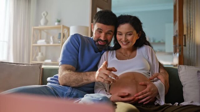 Expecting couple relaxing sofa touching pregnant belly. Parents bonding home.