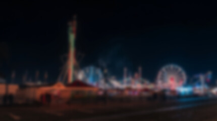 Fototapeta premium Abstract blurry night view of a colorful amusement park with glowing rides and ferris wheel.
