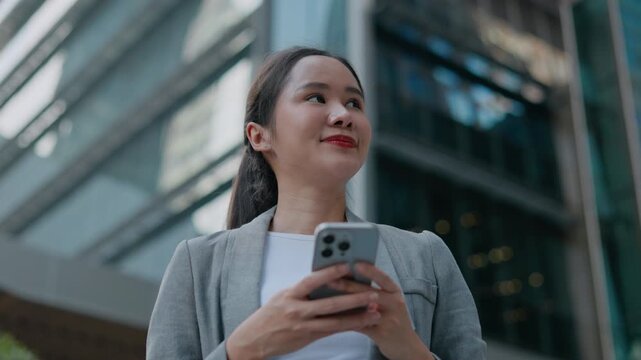 happy successful asian business woman using smartphone in front of modern business building.