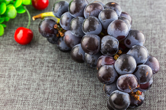 A close-up of a plump dark purple grape bunch paired with bright red cherries, placed on a textured gray fabric surface.