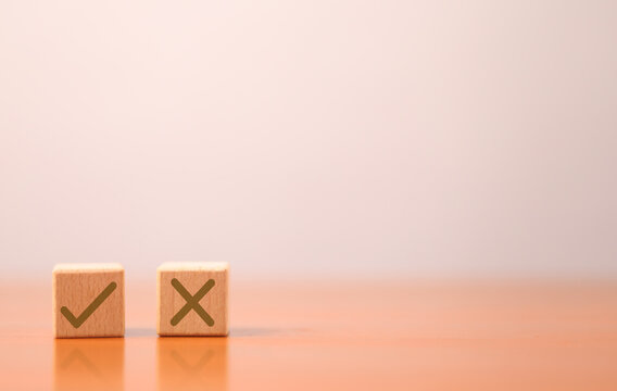 Wooden blocks with check and X symbols on a soft peach background, representing choice, decision, approval, rejection, success, failure, comparison, and evaluation with clean copy space for design.