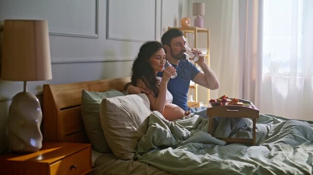 Married couple drinking water breakfast bed. Man embracing pregnant wife home.