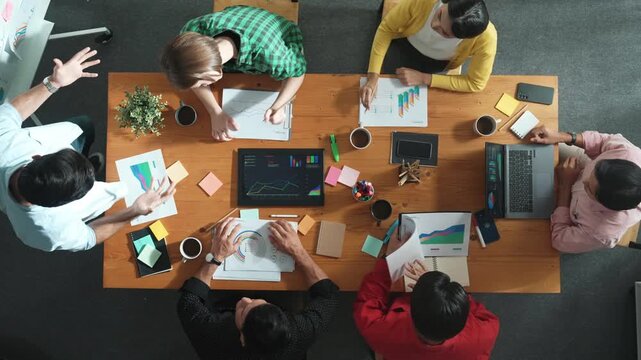 Top down view of investor brainstorming while looking at financial statistic document. Group of diverse people sharing marketing idea or planning marketing campaign with skilled leader. Convocation.